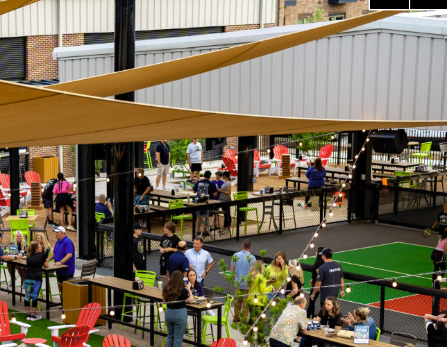 A Chicken N Pickle patio, with courts, string lights, and full seating alongside a bar and dining area